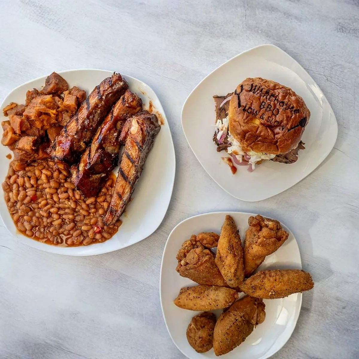 Ribs with baked beans, a pulled pork sandwich on a Warehouse BBQ branded bun, and fried wings